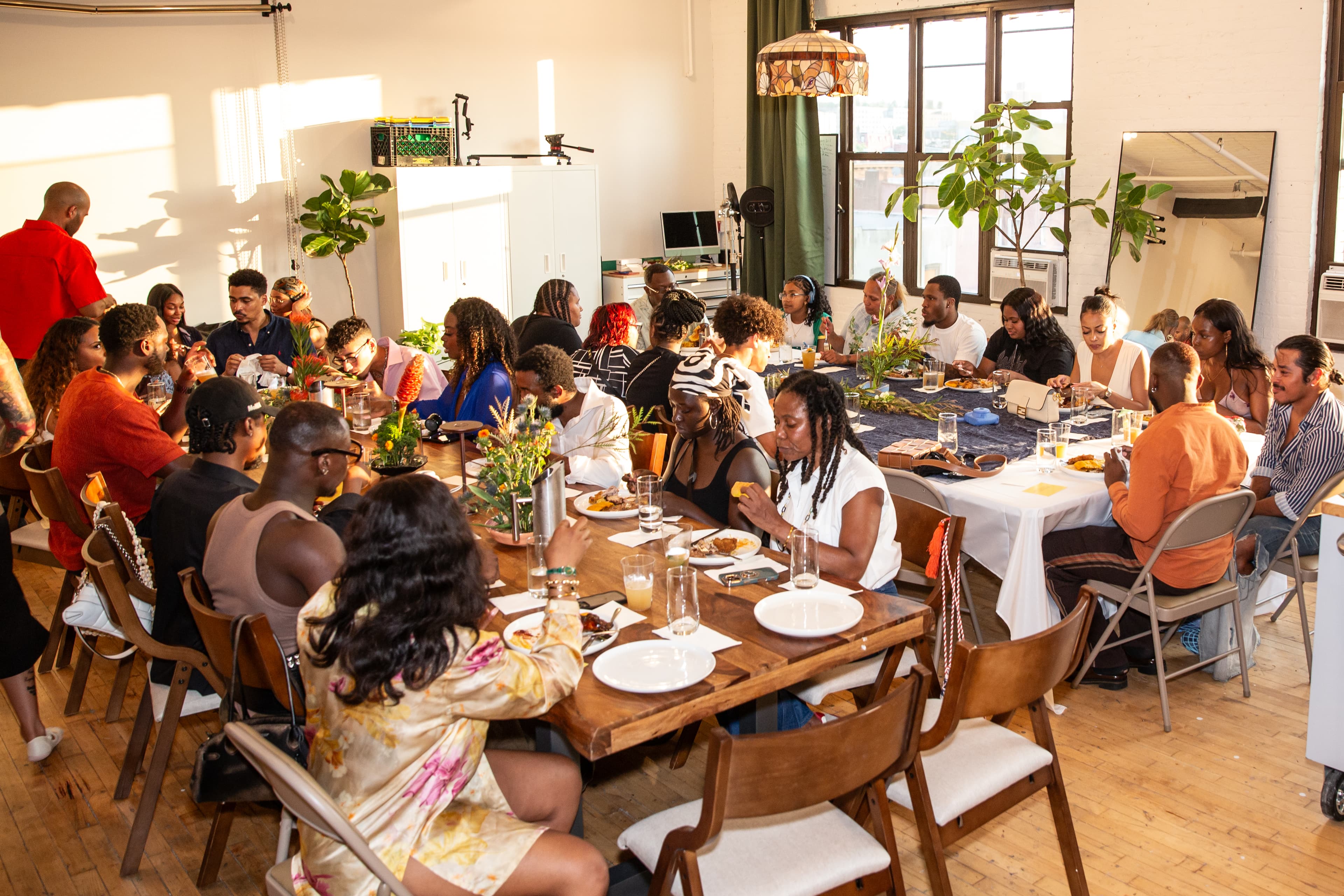 Guests sharing a meal around long tables in the sunlit studio