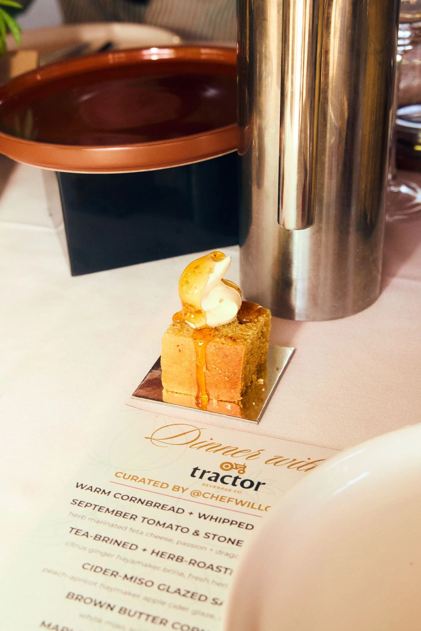 A plated dessert and branded dinner menu beside a sculptural metal vase