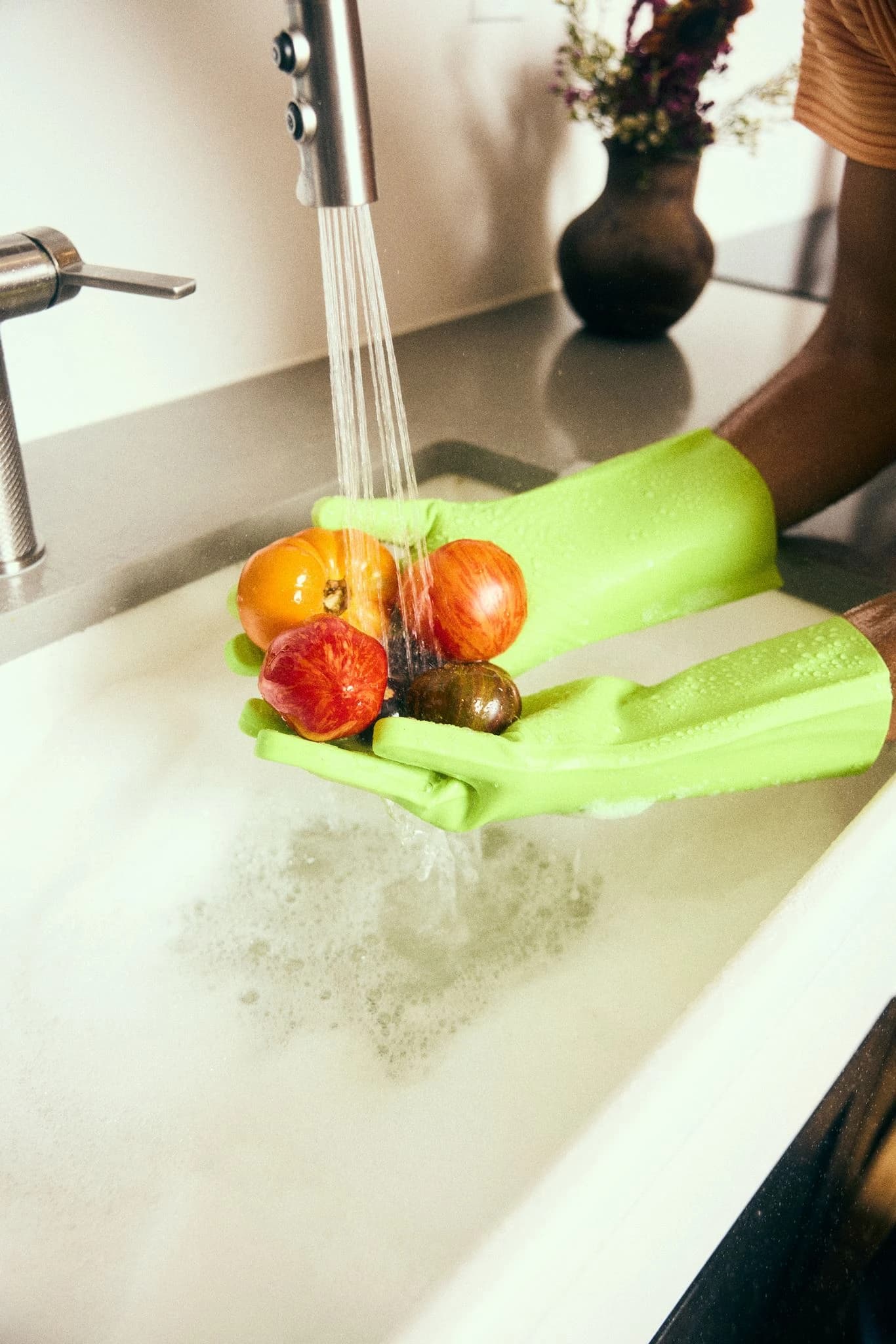 Hands in bright green gloves washing colorful tomatoes under running water in the studio kitchen