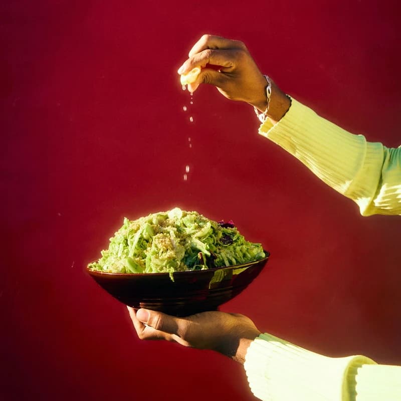 Hands squeezing lemon over a bowl of salad against a red backdrop