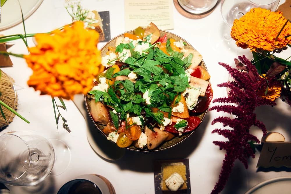 An overhead view of a colorful shared dish surrounded by flowers and glassware