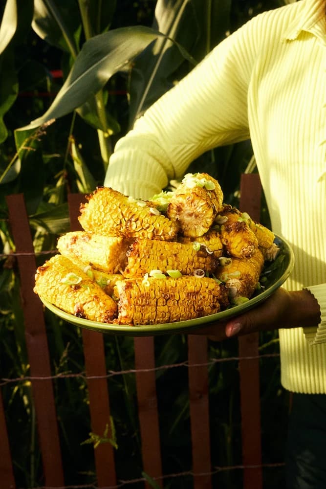 A platter of grilled corn held against a yellow sweater